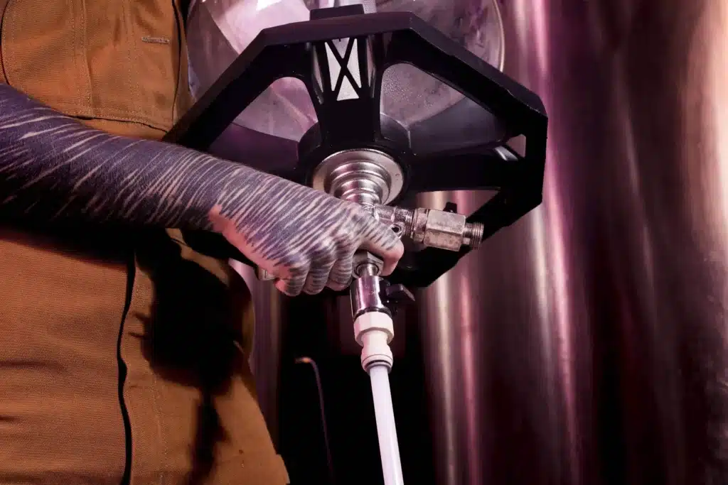 Tattooed brewery worker connecting a hose to stainless steel brewing equipment