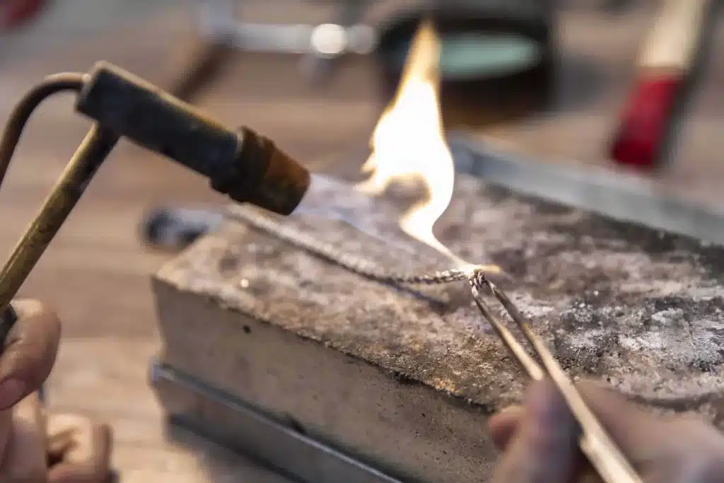 Close-up of a jeweler’s torch heating a metal chain on a soldering block during jewelry making