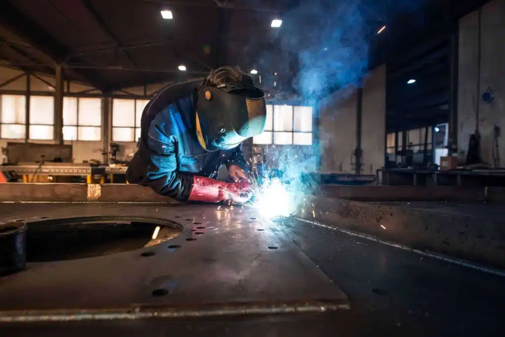 Industrial welder wearing a protective helmet while welding large metal parts in a factory workshop