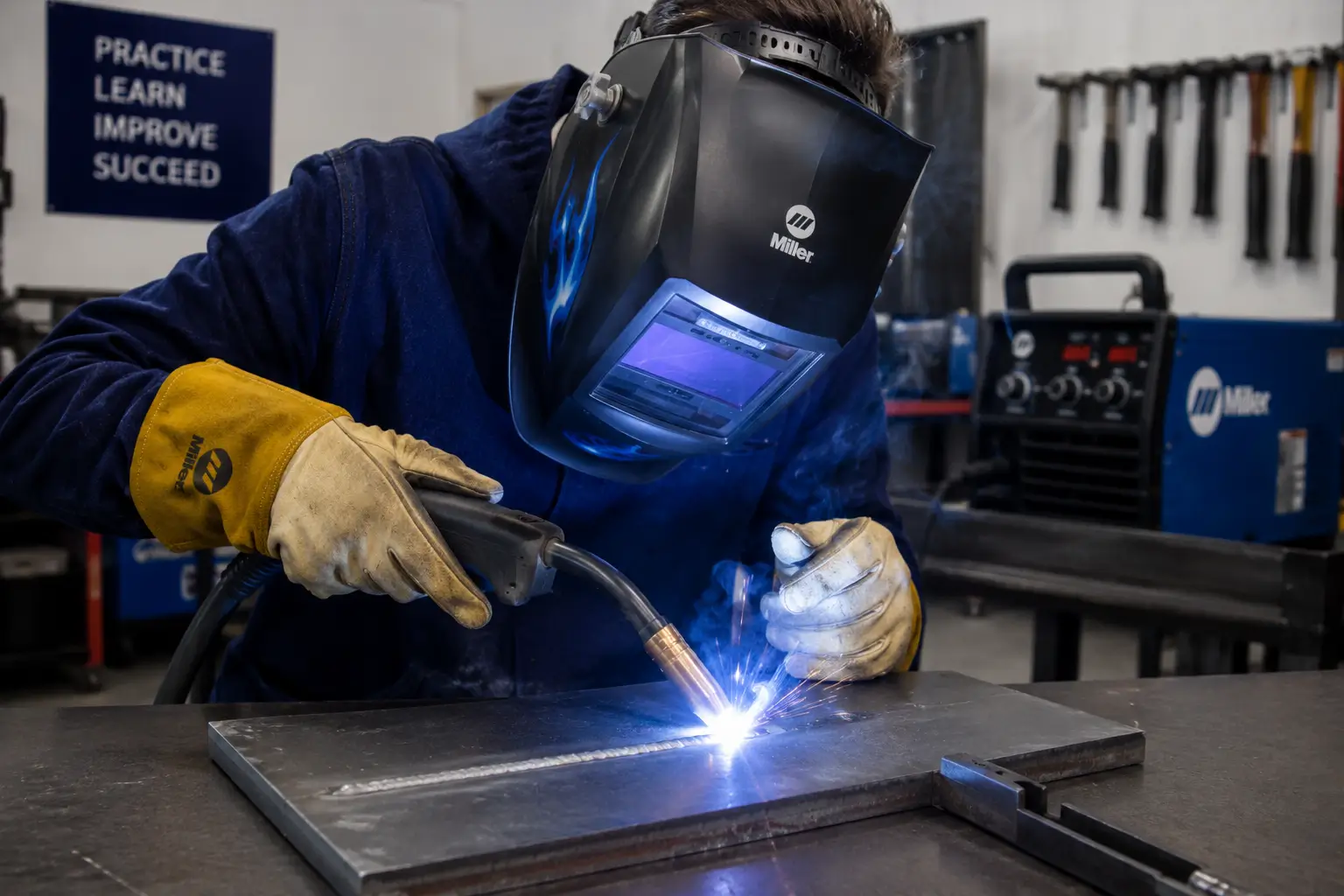 Welder using a MIG welding gun to lay a bead on a steel plate in a workshop.