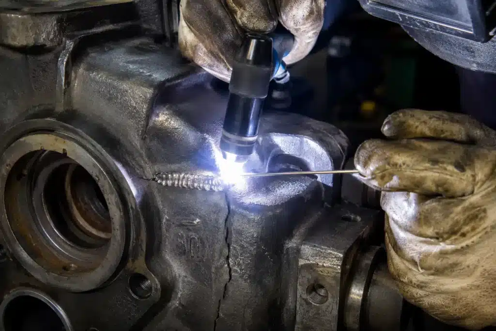 Welder using a TIG torch and filler rod to repair a cracked cast metal component with a controlled weld bead