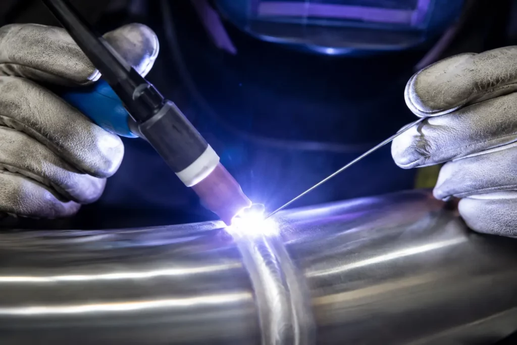 Close-up of a welder using a TIG torch and filler rod to create a clean weld bead on stainless steel tubing.