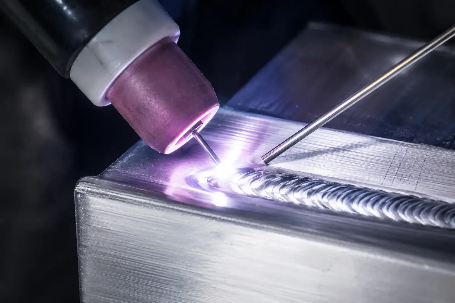 Close-up of a TIG tungsten electrode welding a clean metal bead on aluminum