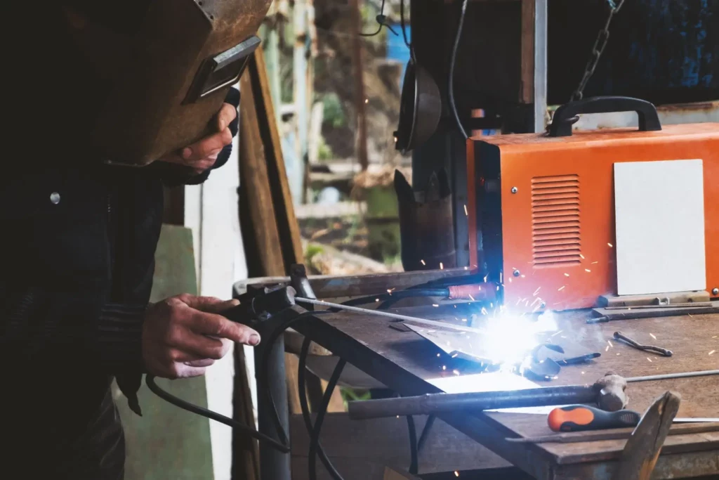 Worker using a portable welding machine on a metal workbench with sparks during light repair work.